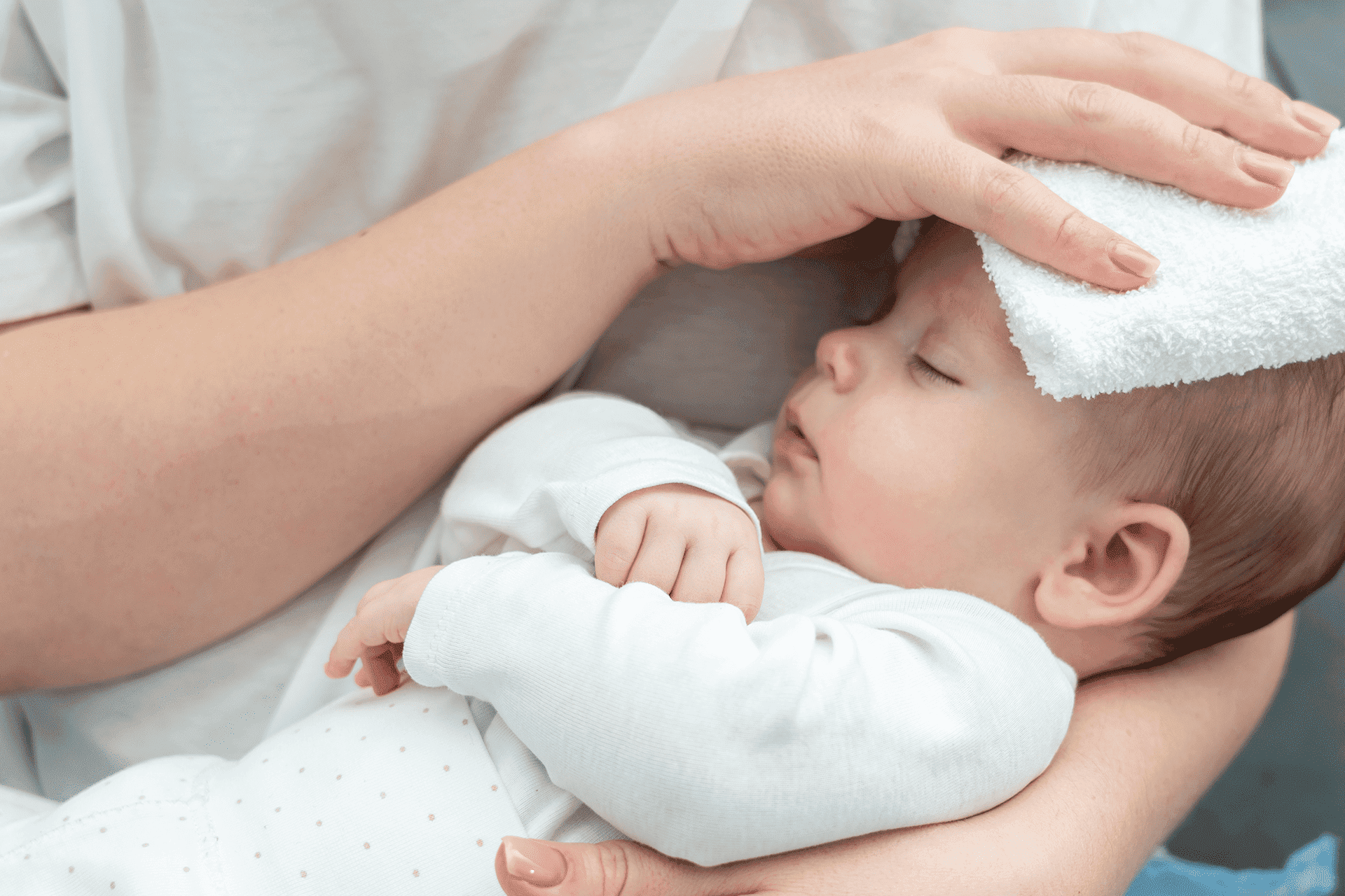 Bebé en brazos mientras le ponen un paño húmedo en su cabeza.